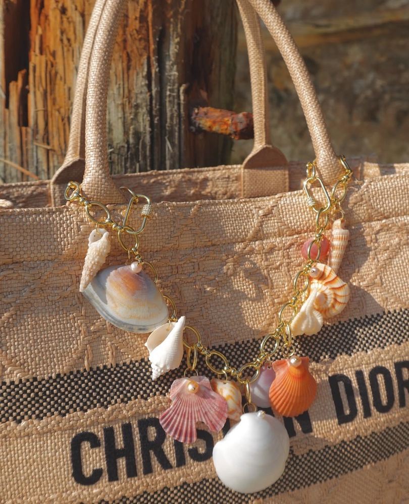 Close-up of a gold shell charm chain on a straw tote against weathered wood
