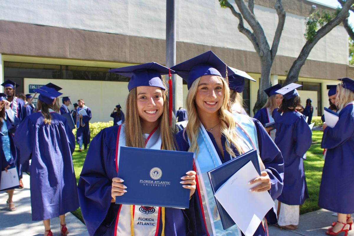 Two graduates smiling with their FAU diploma covers