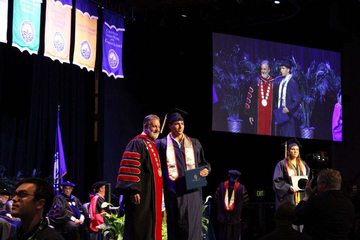 Graduate posing with the university president on stage