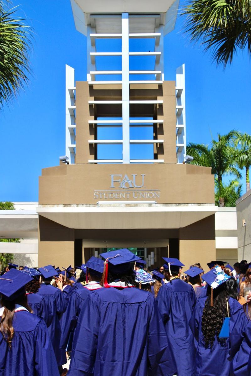 Graduates in caps and gowns walking toward the FAU Student Union