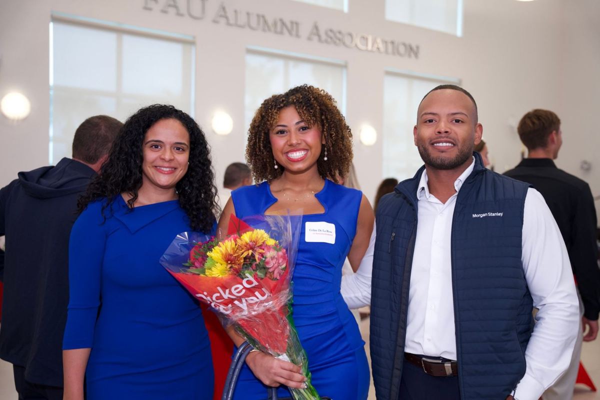 Alumni event guests posing with flowers under the FAU Alumni Association sign