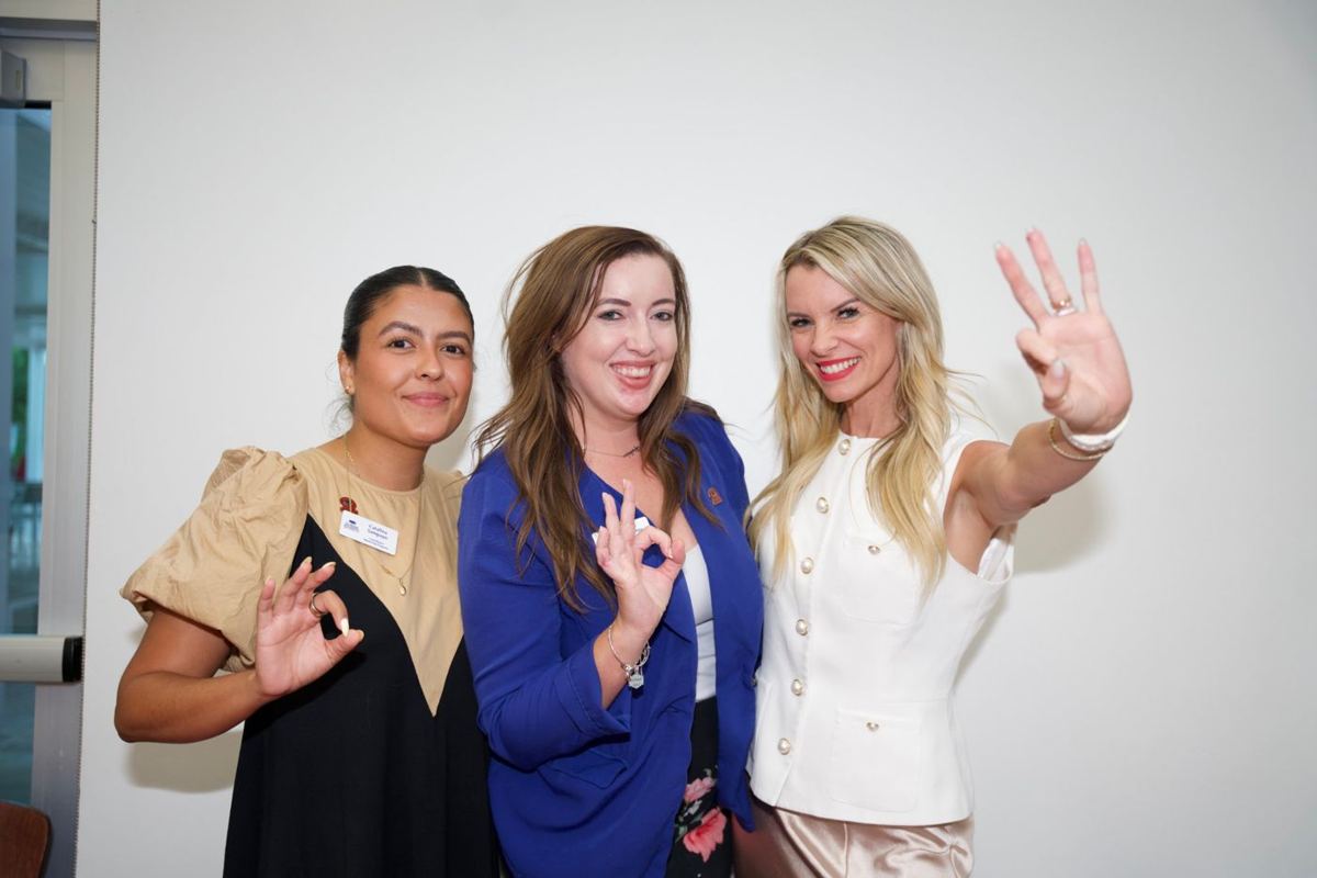 Three women posing with the Owls hand sign at an alumni event